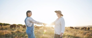 Women farmers shaking hands in a pasture with cattle